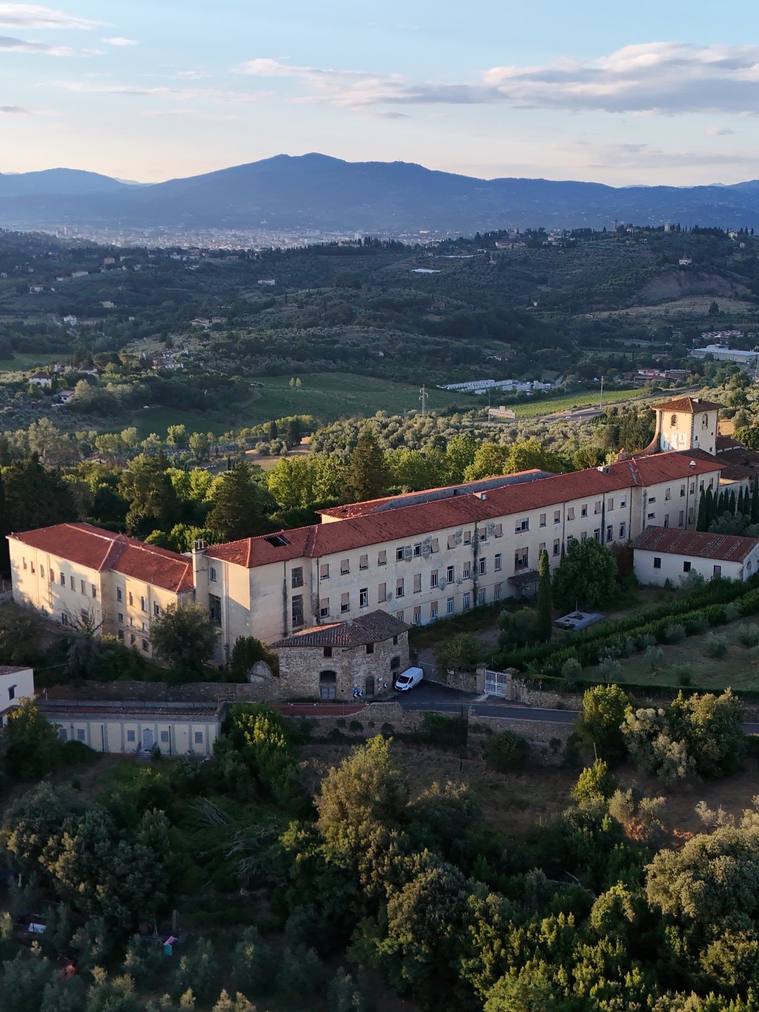 A large historic building on the hills of Florence at sunset, with the city beyond
